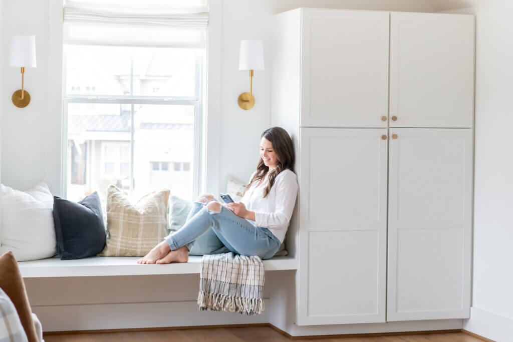 Southern Creative Owner, Steph O'Keefe Working On Keyword Research For Beginners On Phone Wearing A White Shirt And Blue Jeans At Home Office In Raleigh, Nc.