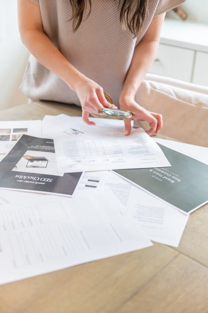 Seo Strategist, Stephanie O'Keefe Holding Magnifying Glass While Looking Through Seo Papers