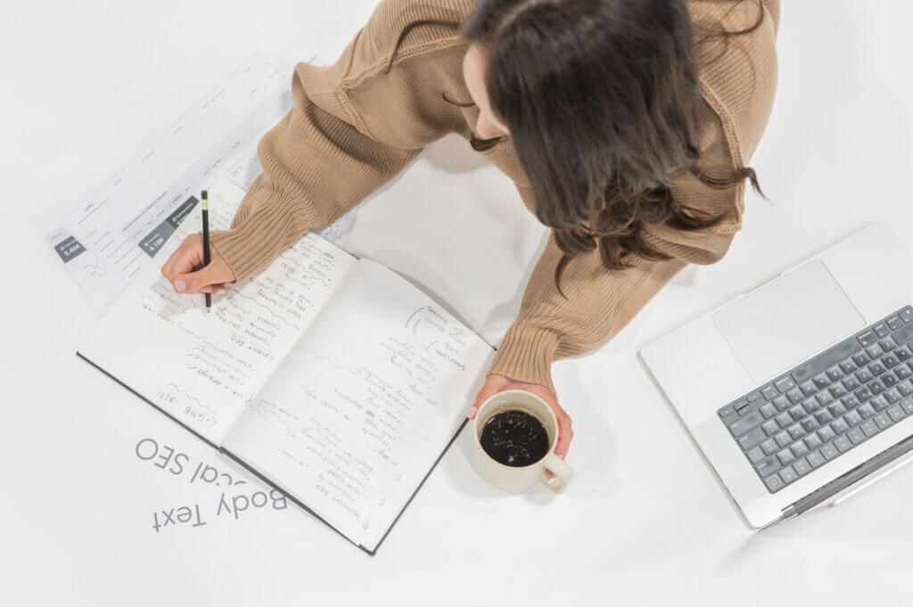 Beaver Builder Vs Elementor: Which One Is Best For Your Business? Stephanie O'Keefe Writing Out Information Comparing Beaver Builder Vs. Elementor On Notebook