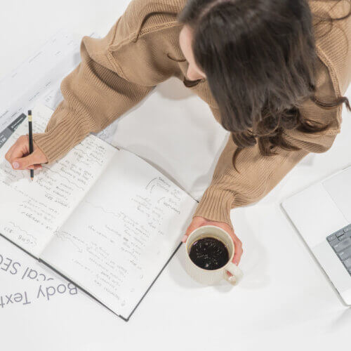 Stephanie O'Keefe writing out information comparing Beaver builder vs. elementor on notebook